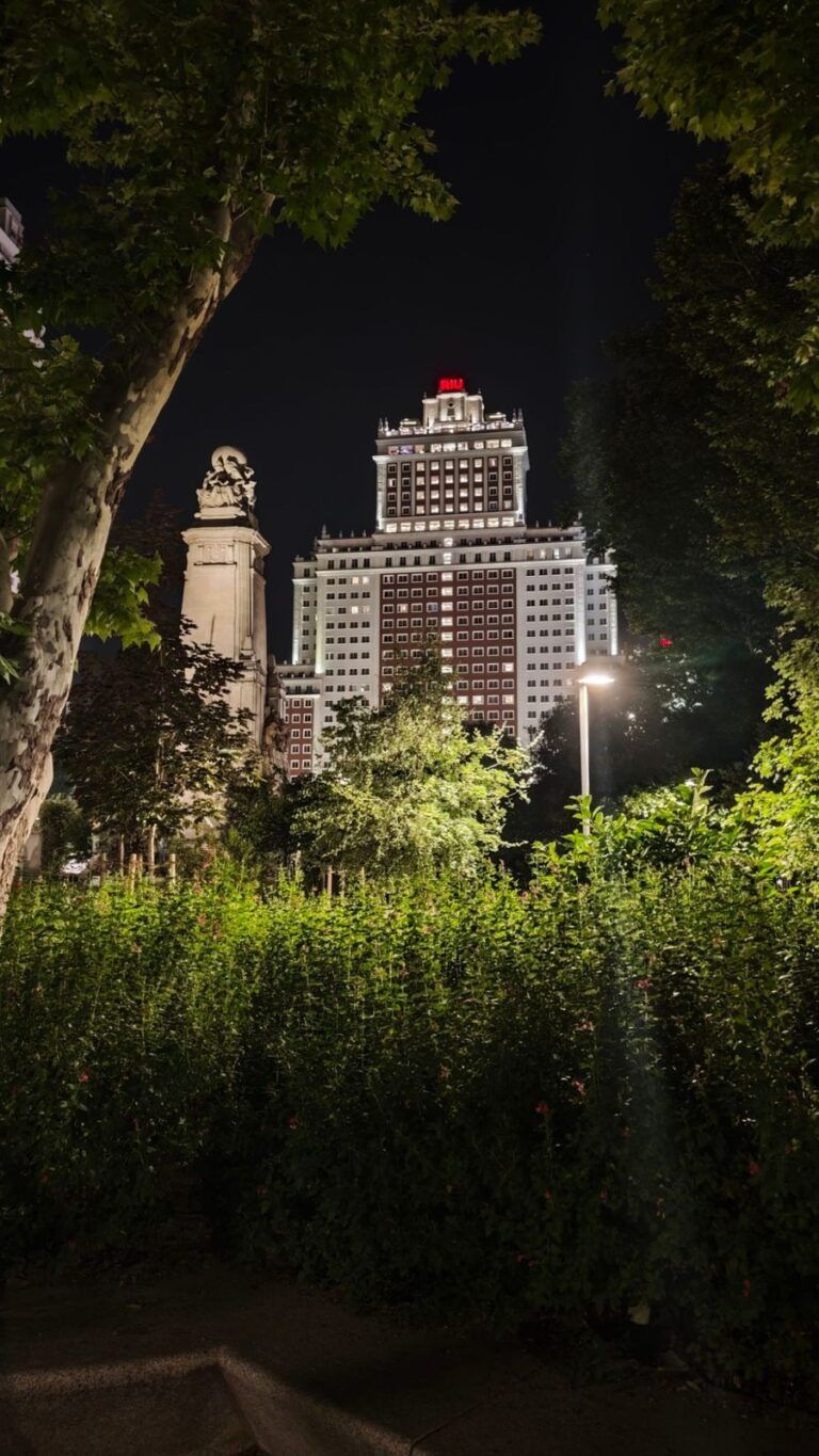 El Edificio España iluminado, visto entre los árboles de la Plaza de España de Madrid